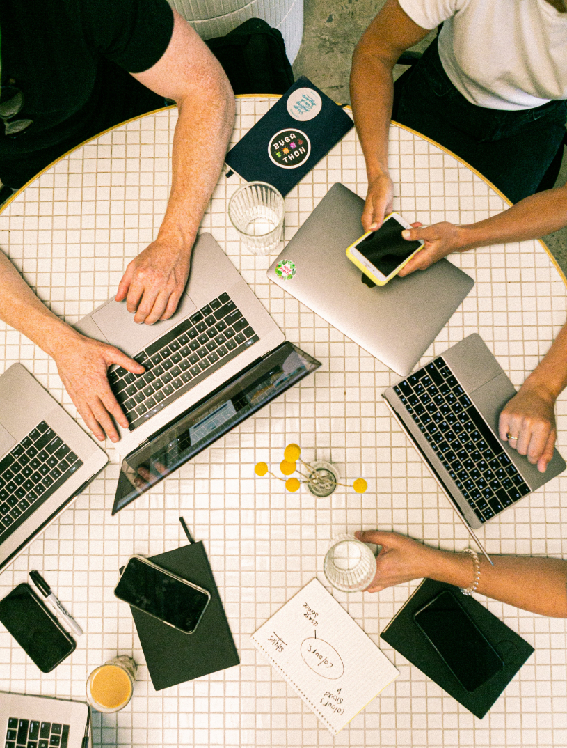 Image looking down on a table with three people working using laptops and phones